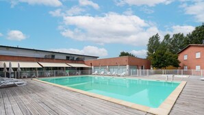 Una piscina con sillones de descanso, una terraza de madera y un edificio de fachada de ladrillo.