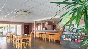 Un área de recepción con mostrador, taburetes de bar, una exhibición de libros y una planta grande.