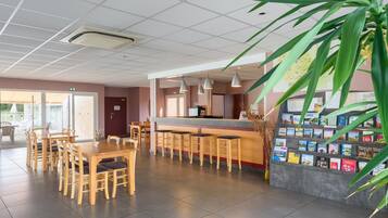 Un espace d’accueil comprenant un comptoir, des tabourets de bar, une étagère où sont exposés des livres et une grande plante.