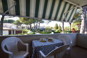 Ein überdachter Außenbereich mit Tisch und Stühlen, Blick auf die umliegende Nachbarschaft und einem gestreiften Markisen.