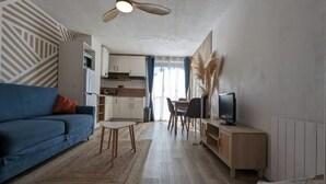 Ein modernes Wohnzimmer mit einer Couch, einem Fernseher, einem Esstisch und einer Küche im Hintergrund.
