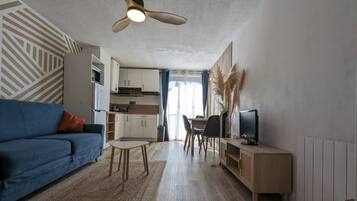 A modern living room with a sofa, a TV, a dining table, and a kitchen in the background.