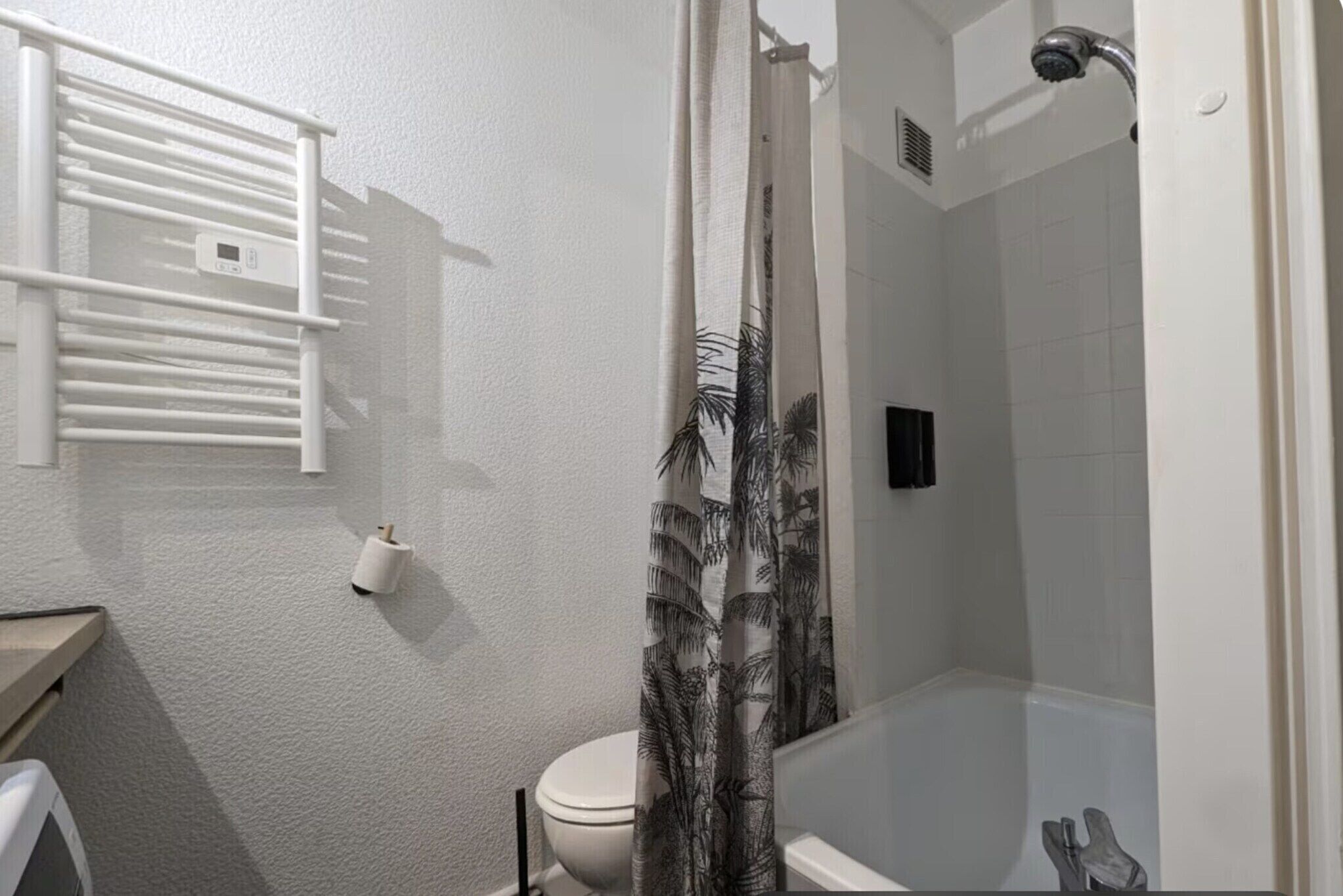 A bathroom with a toilet, a bathtub, a shower curtain with a tropical pattern, and a towel rack.