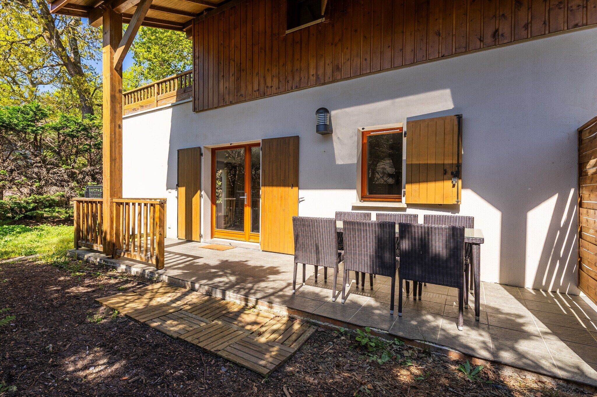 Un bâtiment en bois doté d’un balcon, d’une terrasse couverte avec des meubles en osier et d’une porte avec une fenêtre.