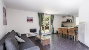 A living room with a sofa, a TV, a glass coffee table, and a dining area with chairs and a kitchen in the background. - Apartment in Lacanau near beach (Lacanau)