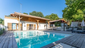 A swimming pool with a wooden deck, a covered seating area, and a building with a sloped roof. - Apartment in Lacanau near beach (Lacanau)