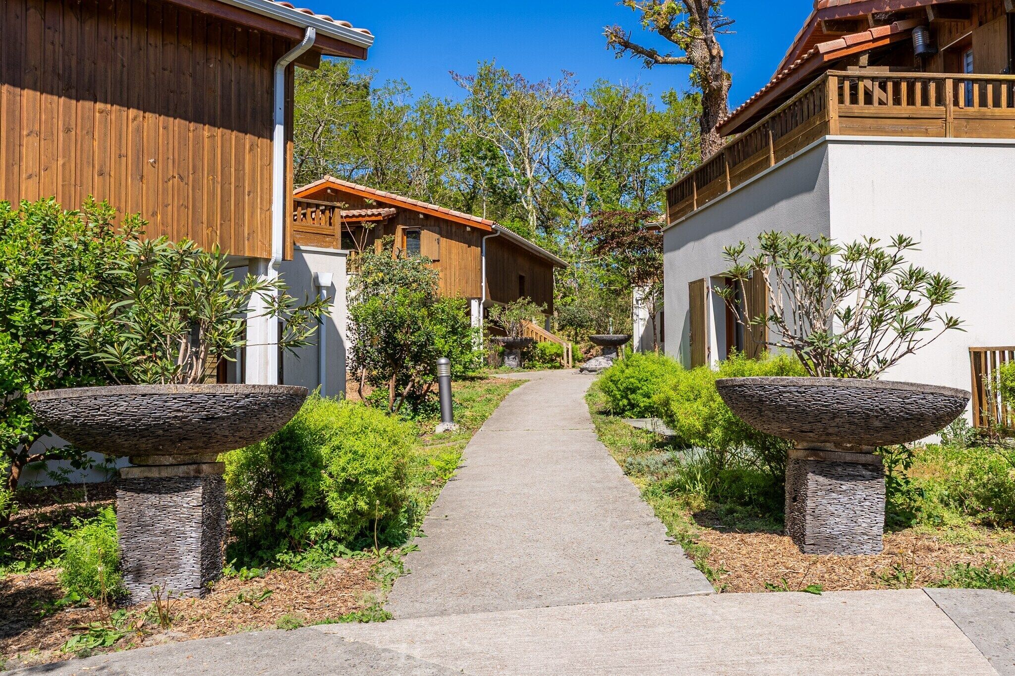 Un chemin menant à un bâtiment doté d’une façade en bois et de jardinières en pierre.