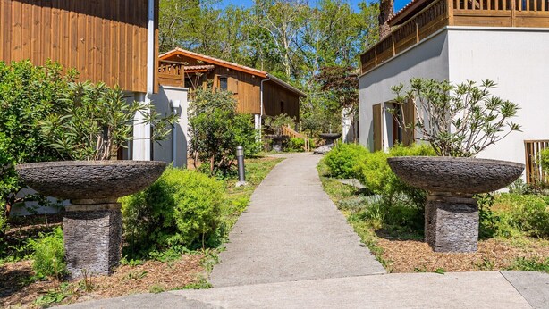A pathway leading to a building with a wooden facade and stone planters. - Apartment in Lacanau near beach (Lacanau)
