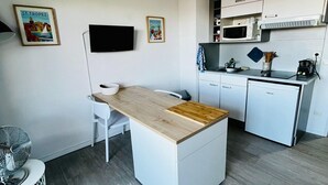 Eine kompakte Küche mit Holzarbeitsplatte, weißen Schränken, einer Mikrowelle, einem kleinen Kühlschrank und einem Fernseher.