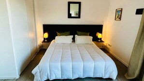 Ein ordentlich bezogenes Bett mit weißer Bettwäsche, zwei Nachttischlampen, ein gerahmtes Bild an der Wand und ein Spiegel über dem Bett.
