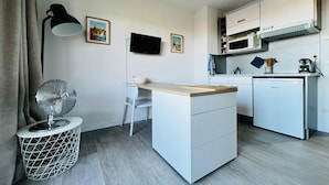 Eine kompakte Küche mit einer kleinen Kochinsel, einer Mikrowelle, einem Geschirrspüler, einem Fernseher und einer Stehlampe.