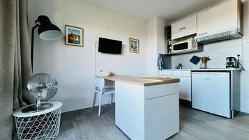 A compact kitchen with a small island, a microwave, a dishwasher, a TV, and a floor lamp.