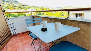 Ein Balkon mit Tisch und Stühlen, Blick auf Grünflächen und Hügel, sowie ein Gebäude im Hintergrund.