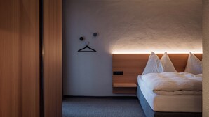 Una camera d'albergo moderna con un letto in legno, una gruccia a parete e un piccolo ripiano.