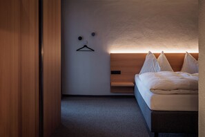 Ein modernes Hotelzimmer mit einem hölzernen Bett, einem Wandhaken und einem kleinen Regal.