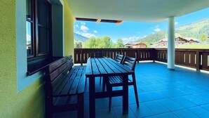 Un balcone con tavolo e panche in legno, vista su un paesaggio montuoso e cielo sereno.