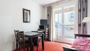 Une pièce comprenant un lit, une table avec des chaises, un téléviseur et une fenêtre avec des rideaux.