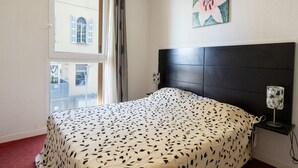 Une chambre à coucher comprenant un lit, une tête de lit, une table de chevet, une lampe, une fenêtre et un tableau.
