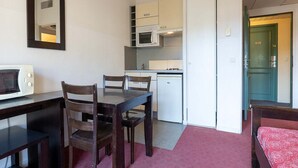 Een compacte kamer met een kitchenette, een eettafel met stoelen, een magnetron en een bed met een rode sprei.