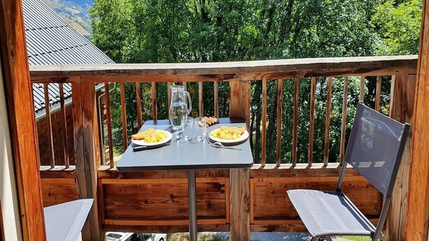 A wooden deck with a table set for two, a chair, and a metal chair. - Alpine Retreat with Balcony and Parking (Saint-Sorlin-d´Arves)