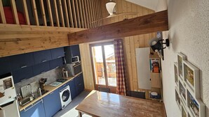 A kitchen with a wooden ceiling, a washing machine, and a dining area with a table. - Alpine Retreat with Balcony and Parking (Saint-Sorlin-d´Arves)
