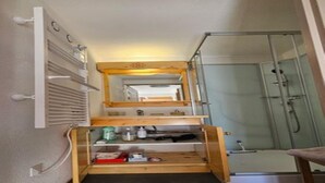 A narrow bathroom with a glass shower enclosure, a built-in shelf with toiletries, and a mirror above the shelf. - Alpine Retreat with Balcony and Parking (Saint-Sorlin-d´Arves)