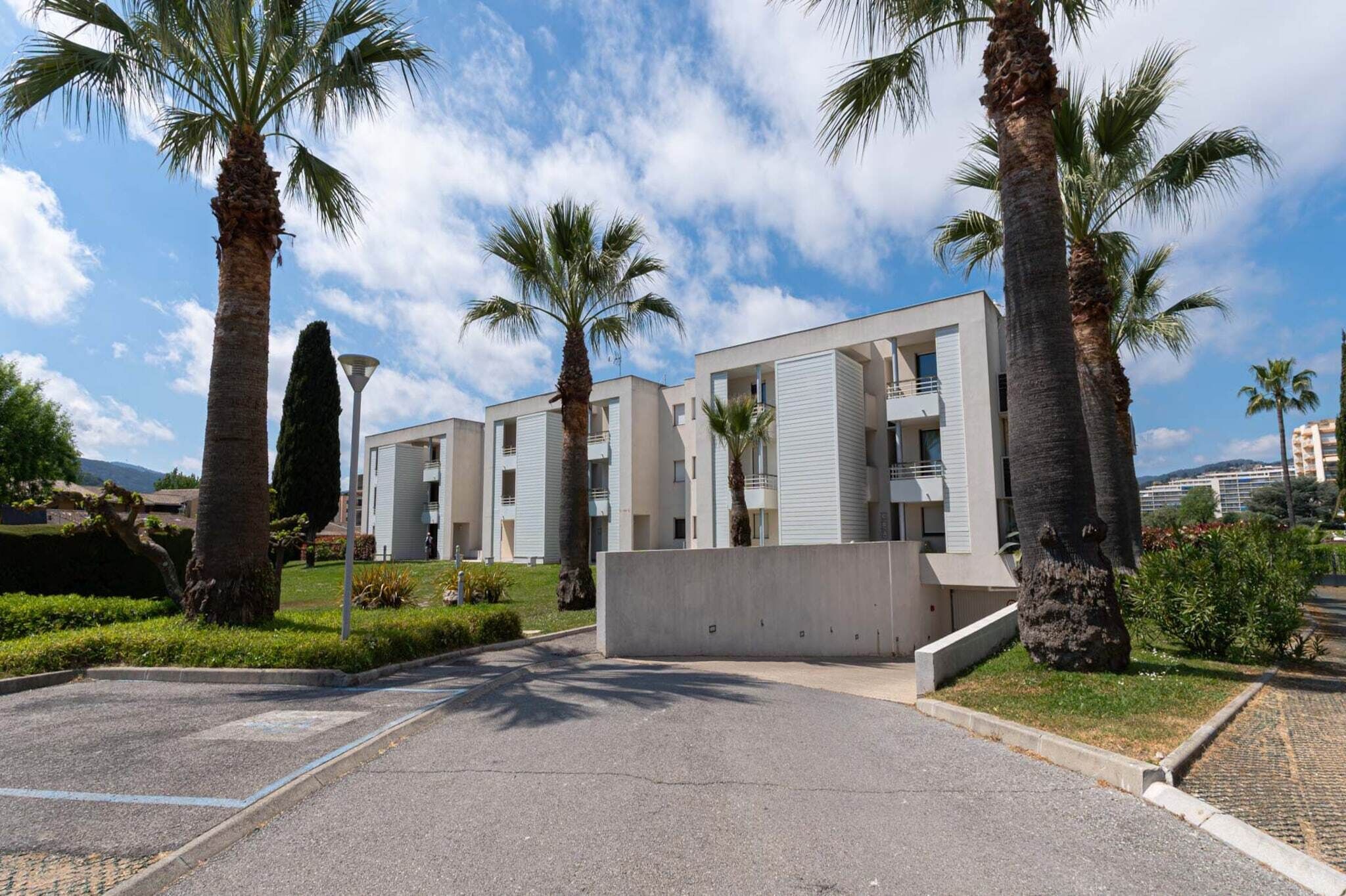 Un immeuble résidentiel moderne doté d’un toit plat, de nombreux balcons et d’un espace de stationnement agrémenté de palmiers.