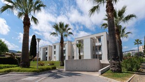 Un edificio residenziale moderno con tetto piatto, numerosi balconi e un'area di parcheggio con palme.