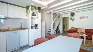 Een moderne keuken met witte kasten, een magnetron en een vaatwasser. Er is een eethoek met een witte tafel en rode stoelen. Een trap leidt naar een andere kamer met een rode bank en een kleine tafel.
