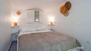 Een slaapkamer met een bed, bedlampjes, een spiegel en een decoratie aan de muur.