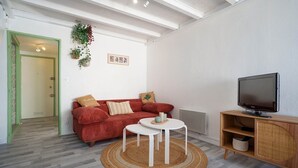 Een woonkamer met een rode bank, een witte salontafel, een televisie op een houten dressoir en een geweven vloerkleed.