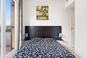 A bedroom with a large bed, a painting above the bed, and a view through a window. - Apartment in Grasse with Pool View (Grasse)