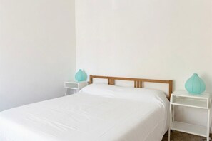 Un letto singolo con una testiera in legno, biancheria da letto bianca e due comodini bianchi con vasi color acquamarina.