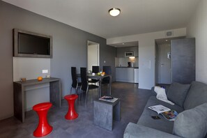 Un salon moderne avec un canapé gris, des tabourets rouges, une petite table basse et un téléviseur à écran plat fixé au mur.