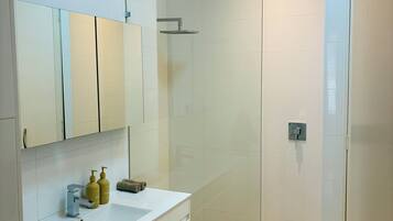Un bagno moderno con box doccia in vetro, un mobile lavabo bianco e uno specchio sopra il mobile.