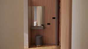 Un pasillo estrecho con una puerta de madera, un pequeño contenedor de basura y un espejo en la pared.
