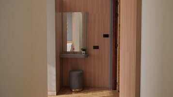 Un pasillo estrecho con una puerta de madera, un pequeño contenedor de basura y un espejo en la pared.