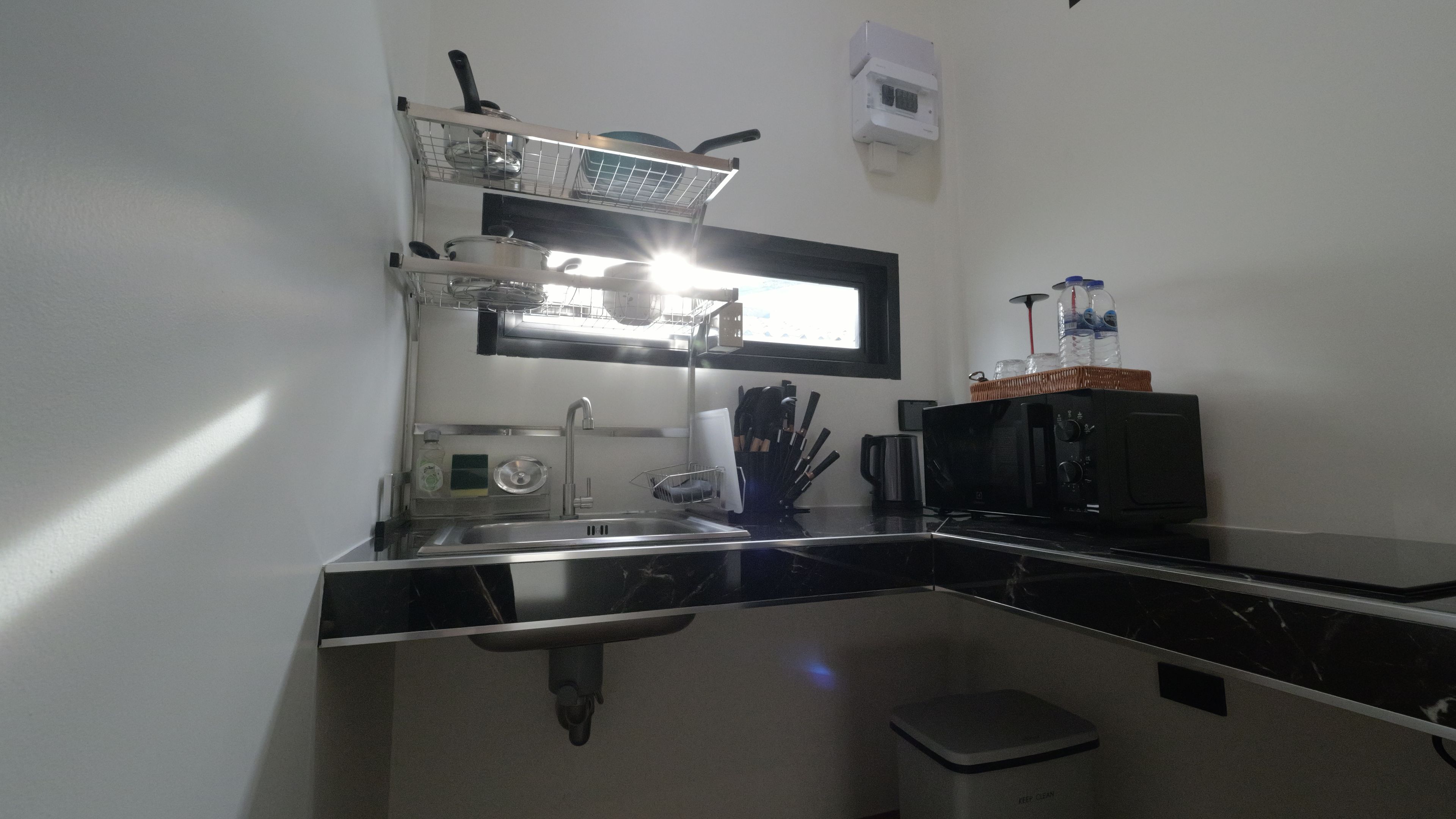 Una cocina compacta con microondas, lavamanos y un pequeño cubo de basura.