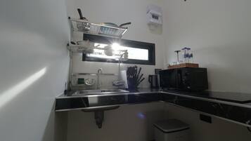 Una cocina compacta con microondas, lavamanos y un pequeño cubo de basura.