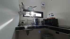 Una cocina compacta con microondas, lavamanos y un pequeño cubo de basura.