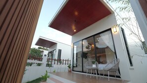 Ein modernes Haus mit einer großen Glasfassade, einer Holzterrasse und Sitzgelegenheiten im Freien.