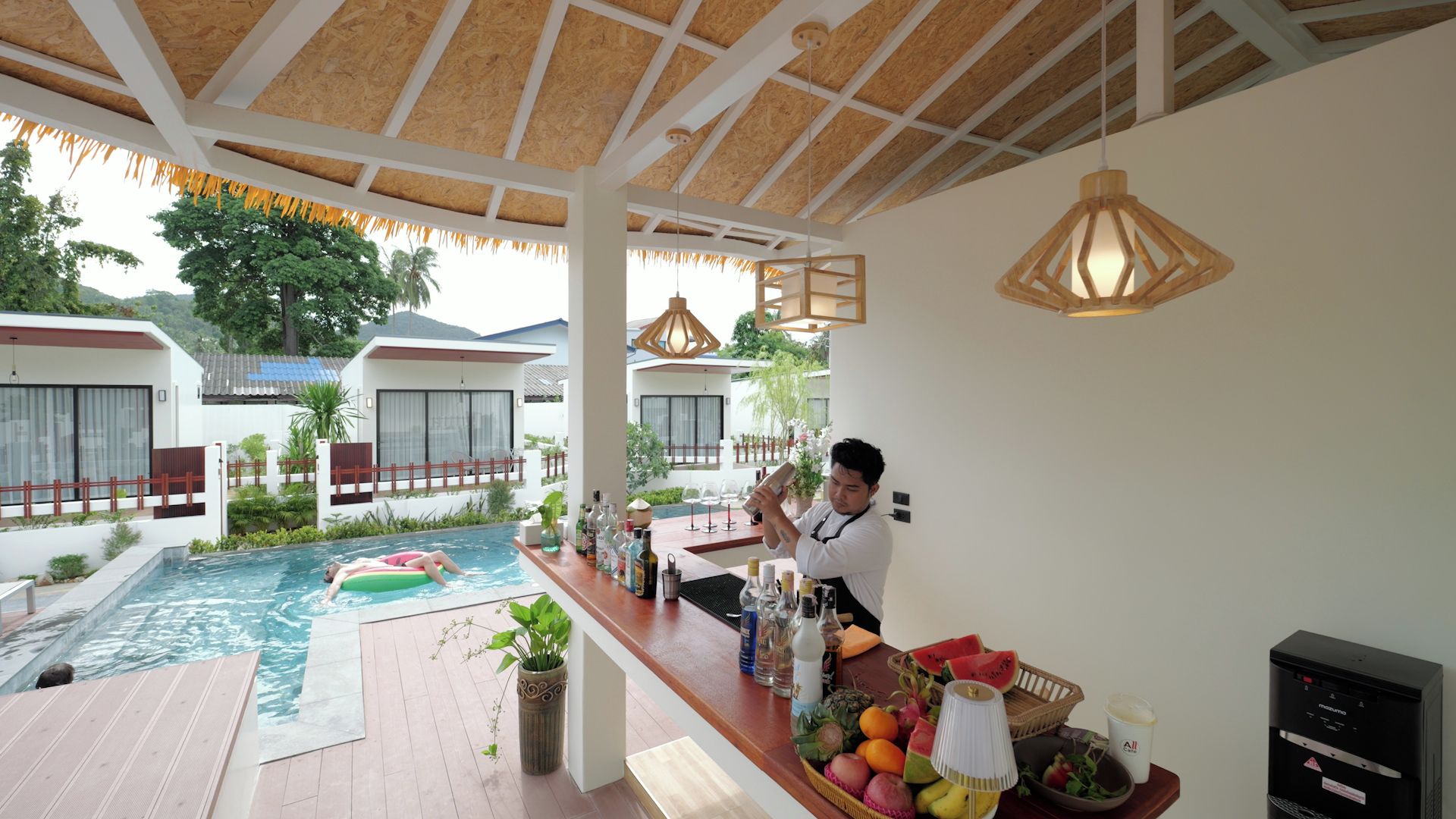 Zona de bar junto a la piscina con un bartender, una piscina y vistas a una zona residencial.