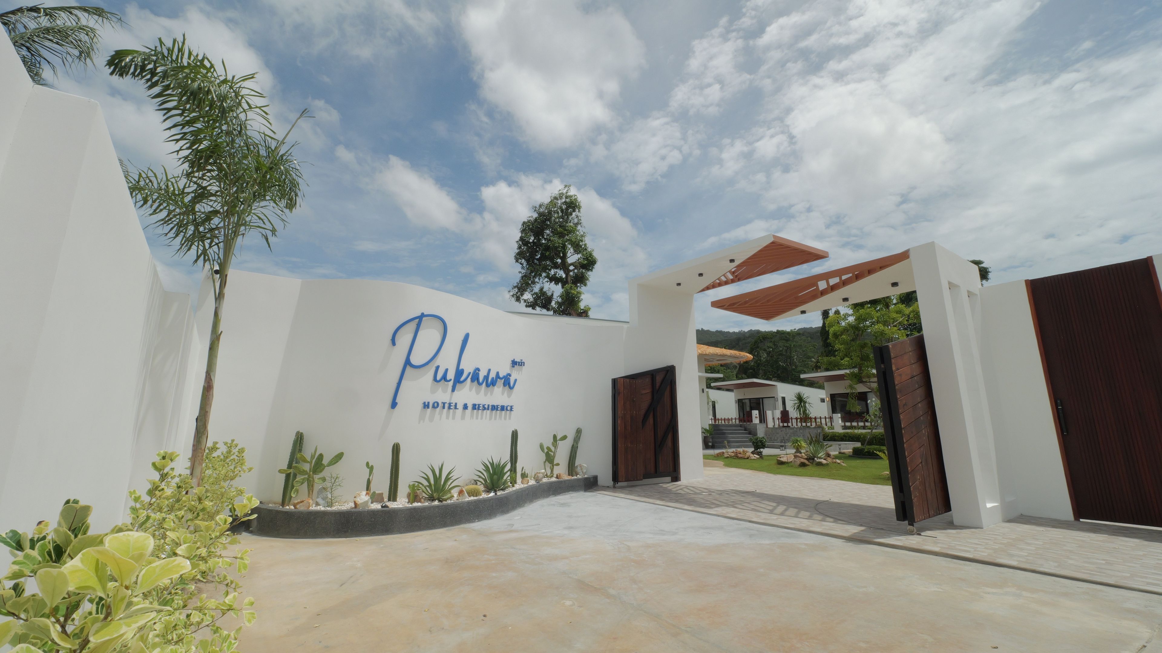 A hotel entrance with a modern design, featuring a large sign, a covered walkway, and a landscaped area with cacti and shrubs.