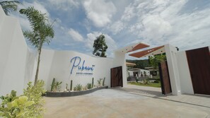 A hotel entrance with a modern design, featuring a large sign, a covered walkway, and a landscaped area with cacti and shrubs. - Pukawa Hotel & Residence (Ko Pha-ngan)