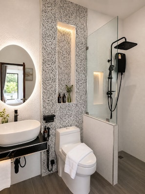 Un baño moderno con un espejo redondo, lavabo blanco, inodoro y ducha con cabina de vidrio.
