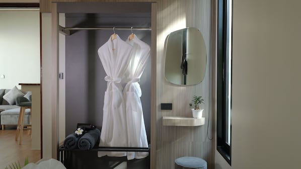 A modern bathroom with a robe hanging, a towel rack, a mirror, a small sink, and a potted plant. - Pukawa Hotel & Residence (Ko Pha-ngan)