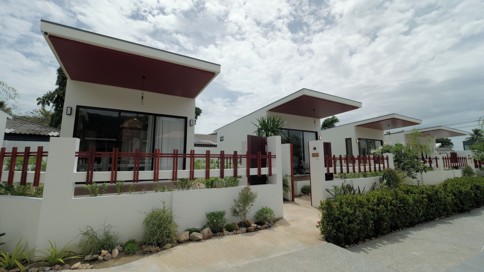 A modern two-story residential building with a flat roof, large windows, and a red fence.