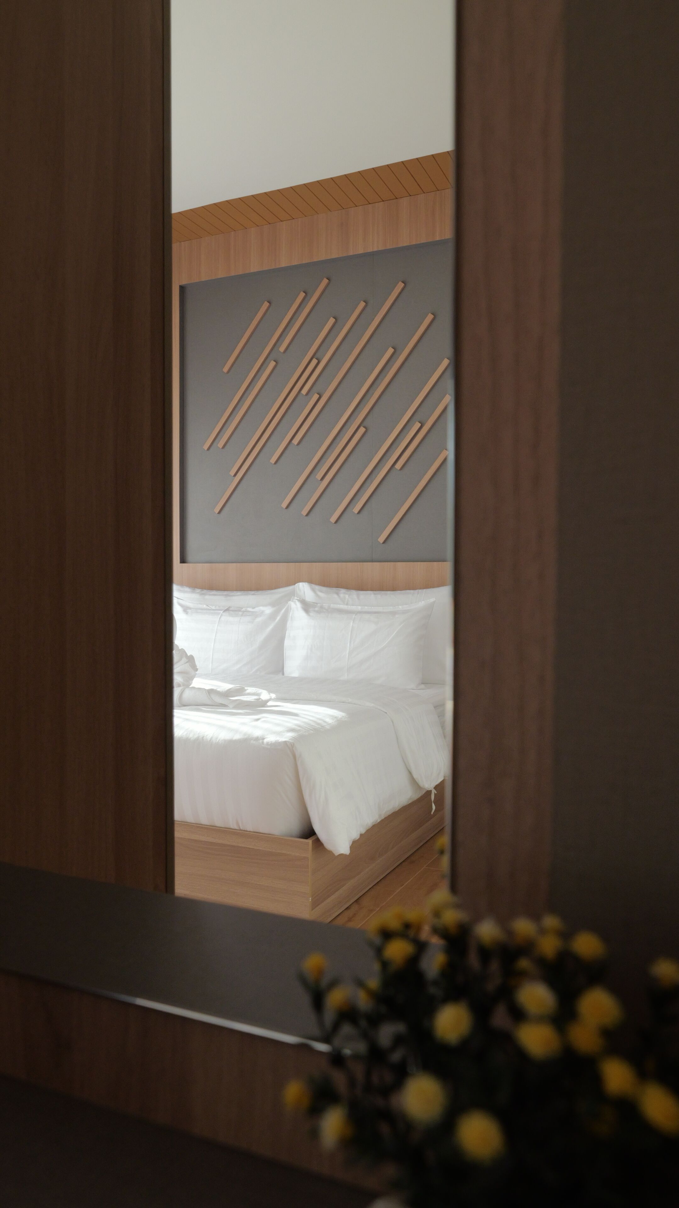 Un dormitorio con cabecera de madera, una cama con ropa de cama blanca y un espejo que refleja la habitación.
