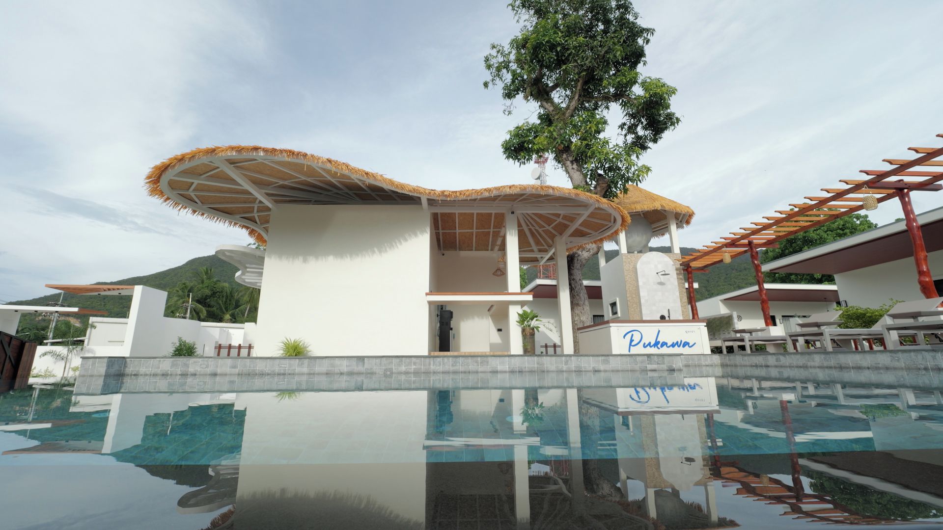 Um hotel moderno com piscina, uma construção com telhado de palha e uma placa com a inscrição 'Pukawa'.