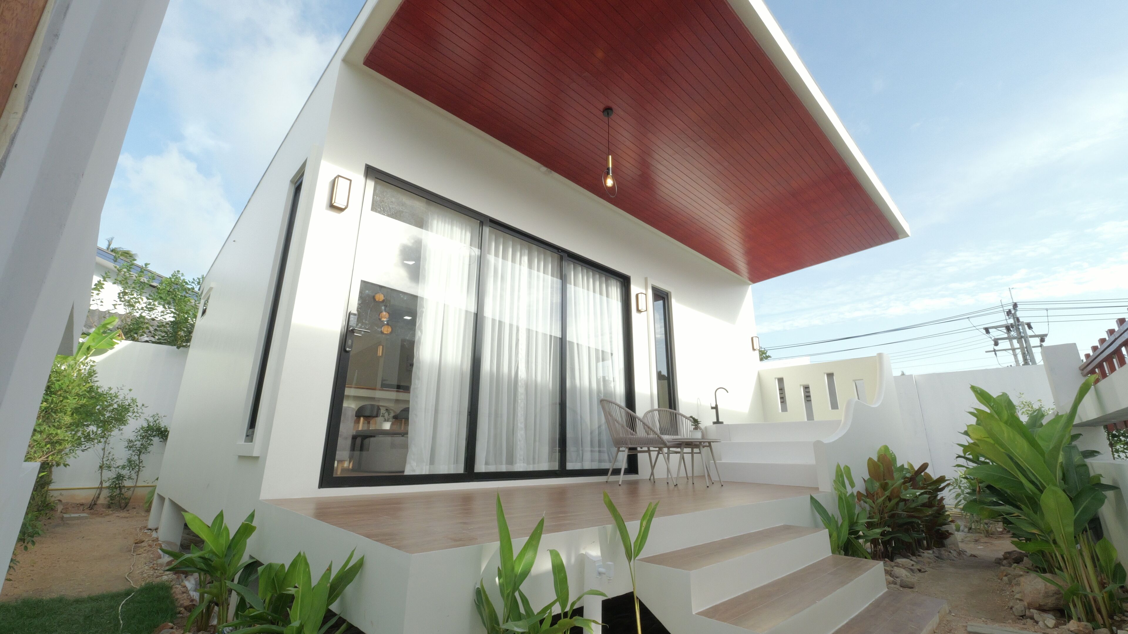 Una casa moderna con techo rojo, grandes puertas correderas de vidrio y una terraza de madera.